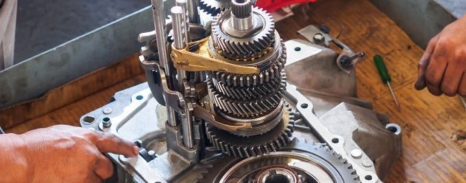 Hands repairing exposed gears inside a metal gearbox on a workbench