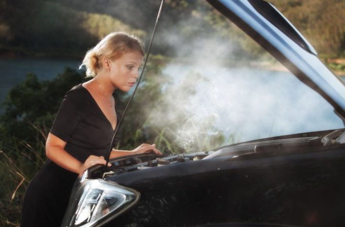 Person inspecting a smoking car engine with the hood open at night