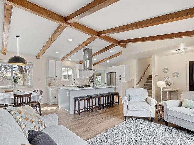 Open-concept kitchen and living room with white walls, exposed wooden beams, and a gray rug.