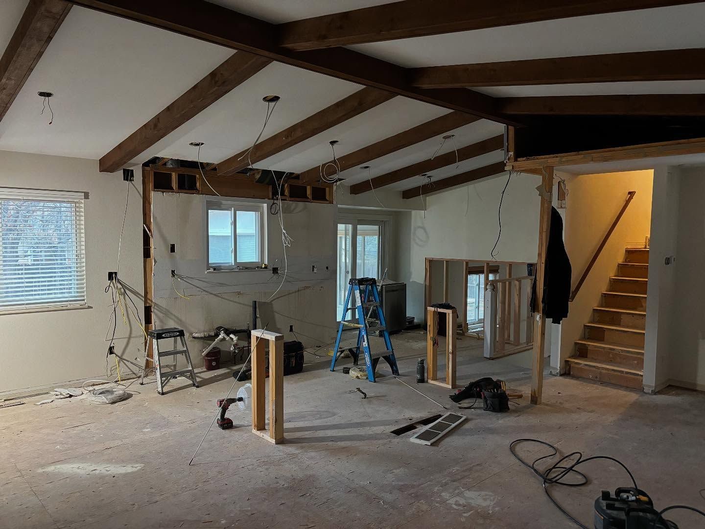 Interior room under construction, exposed beams and wiring, unfinished walls, tools and ladder present.
