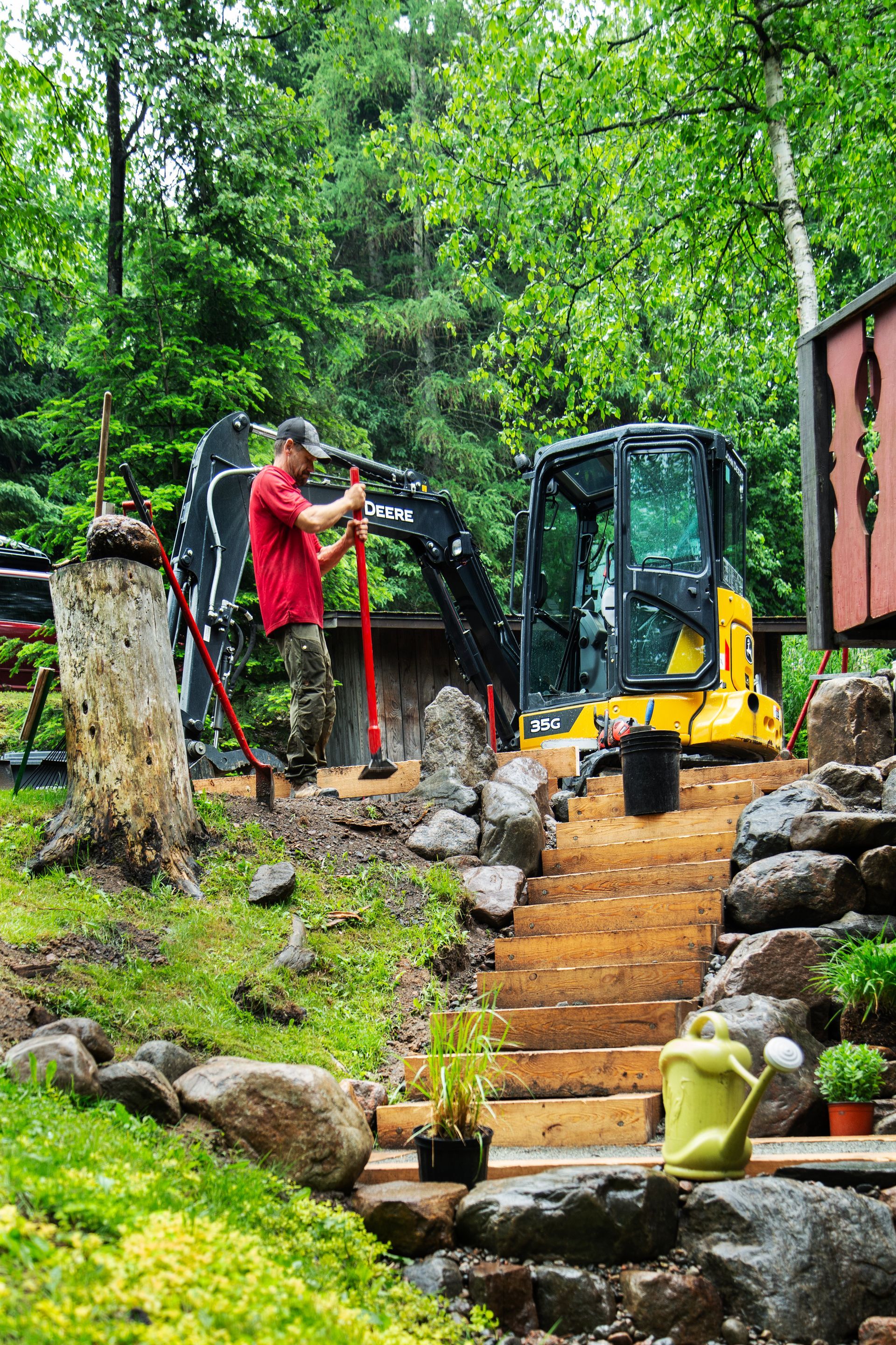 Un homme se tient debout à côté d'une excavatrice jaune dans un jardin.