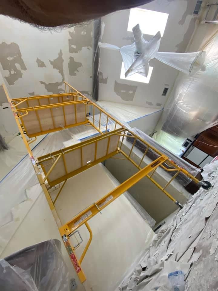 Yellow scaffolding inside a damaged room with peeling walls and exposed plastic sheeting