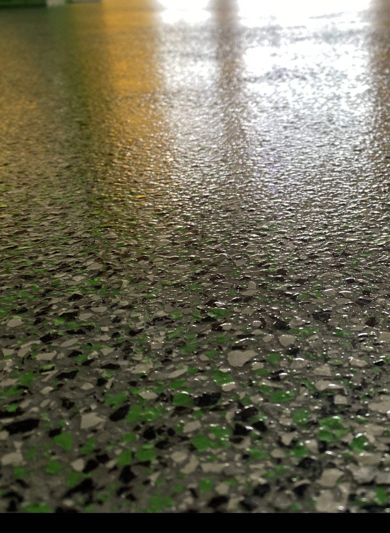 Close-up of a wet speckled floor reflecting light and yellow columns in the background