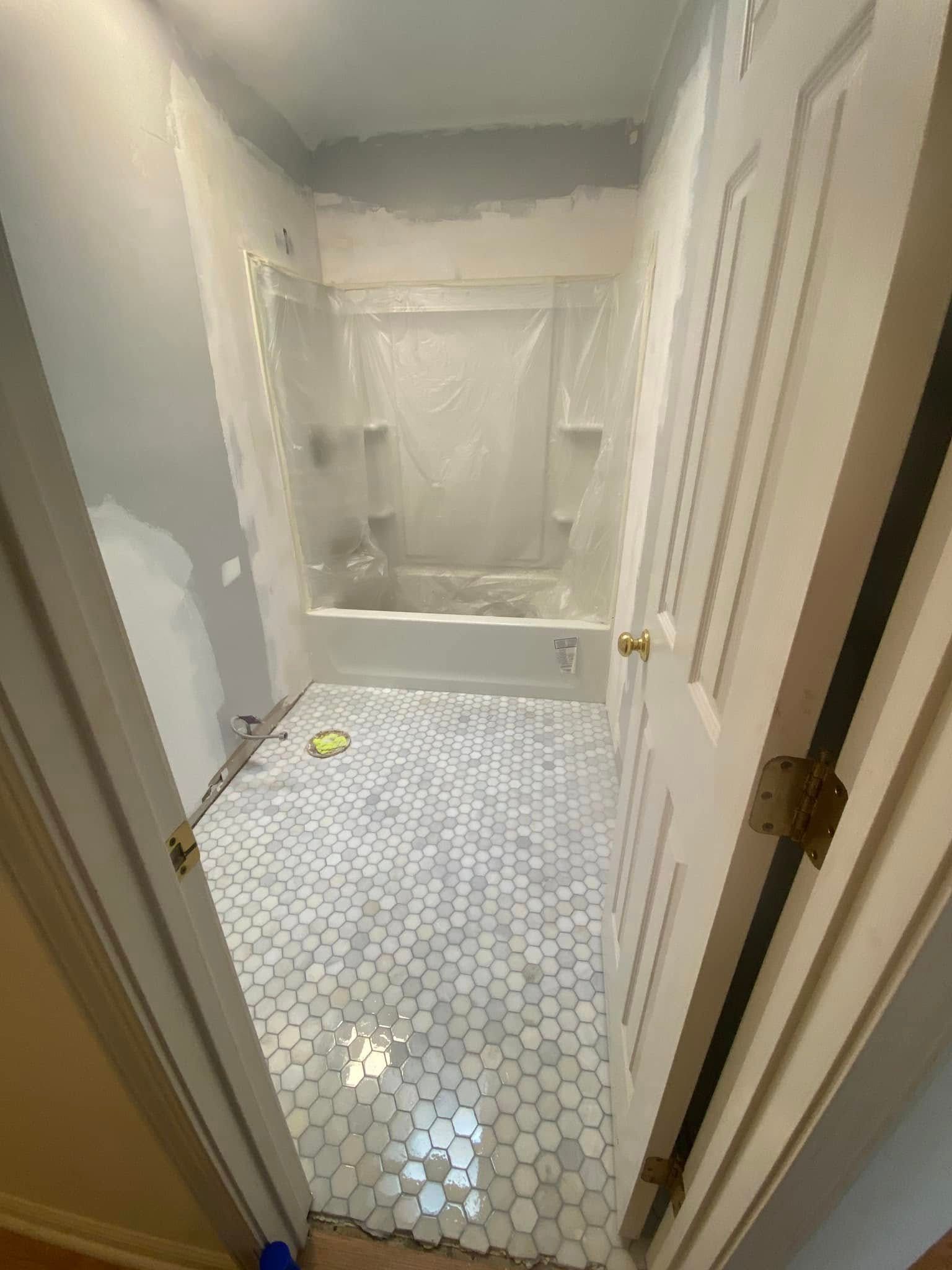 Narrow bathroom under renovation with tiled floor, unfinished walls, and a tub/shower at the back.