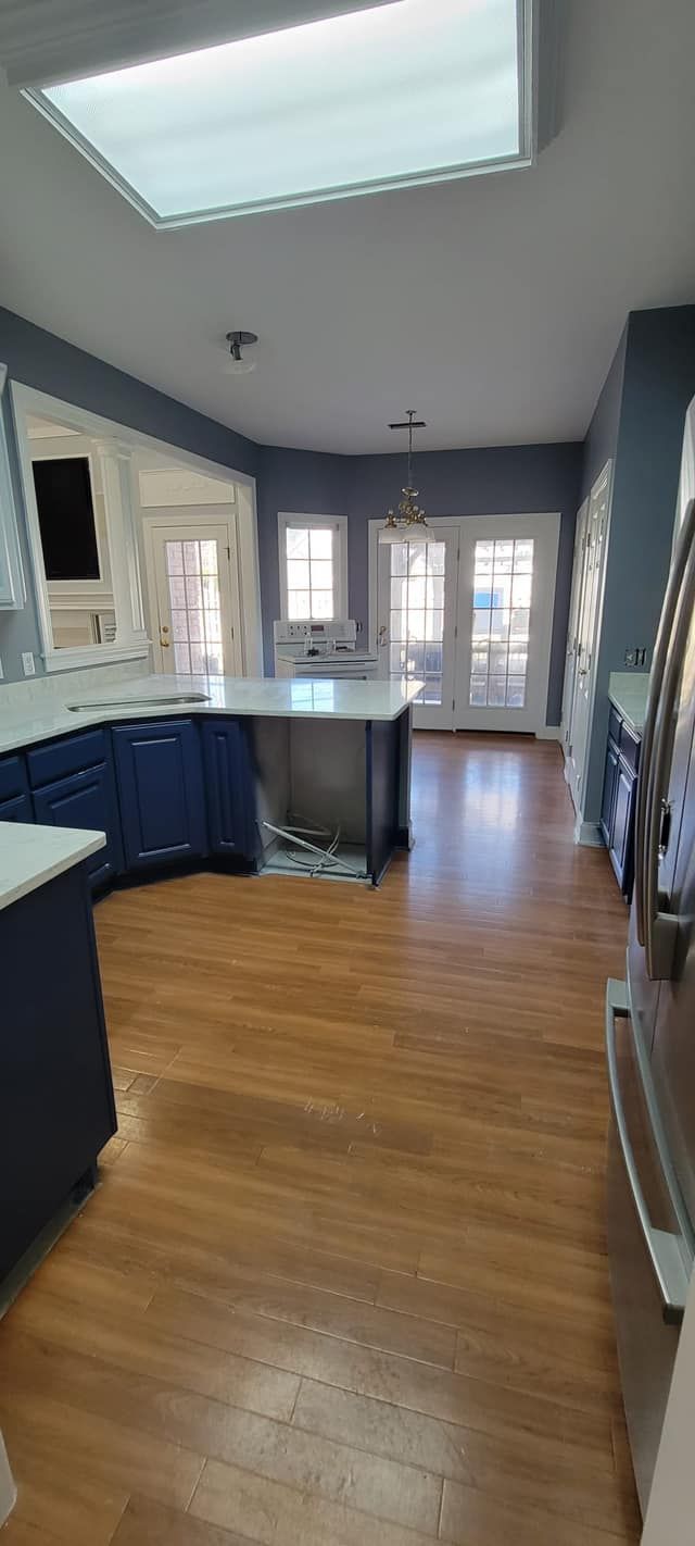 Bright kitchen with blue cabinets, hardwood floors, skylight, and French doors.