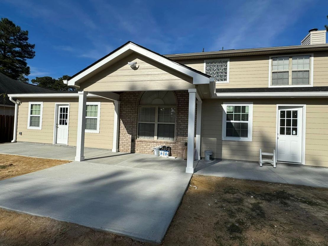 Front view of a beige house with a covered carport, concrete driveway, and white door under a blue sky