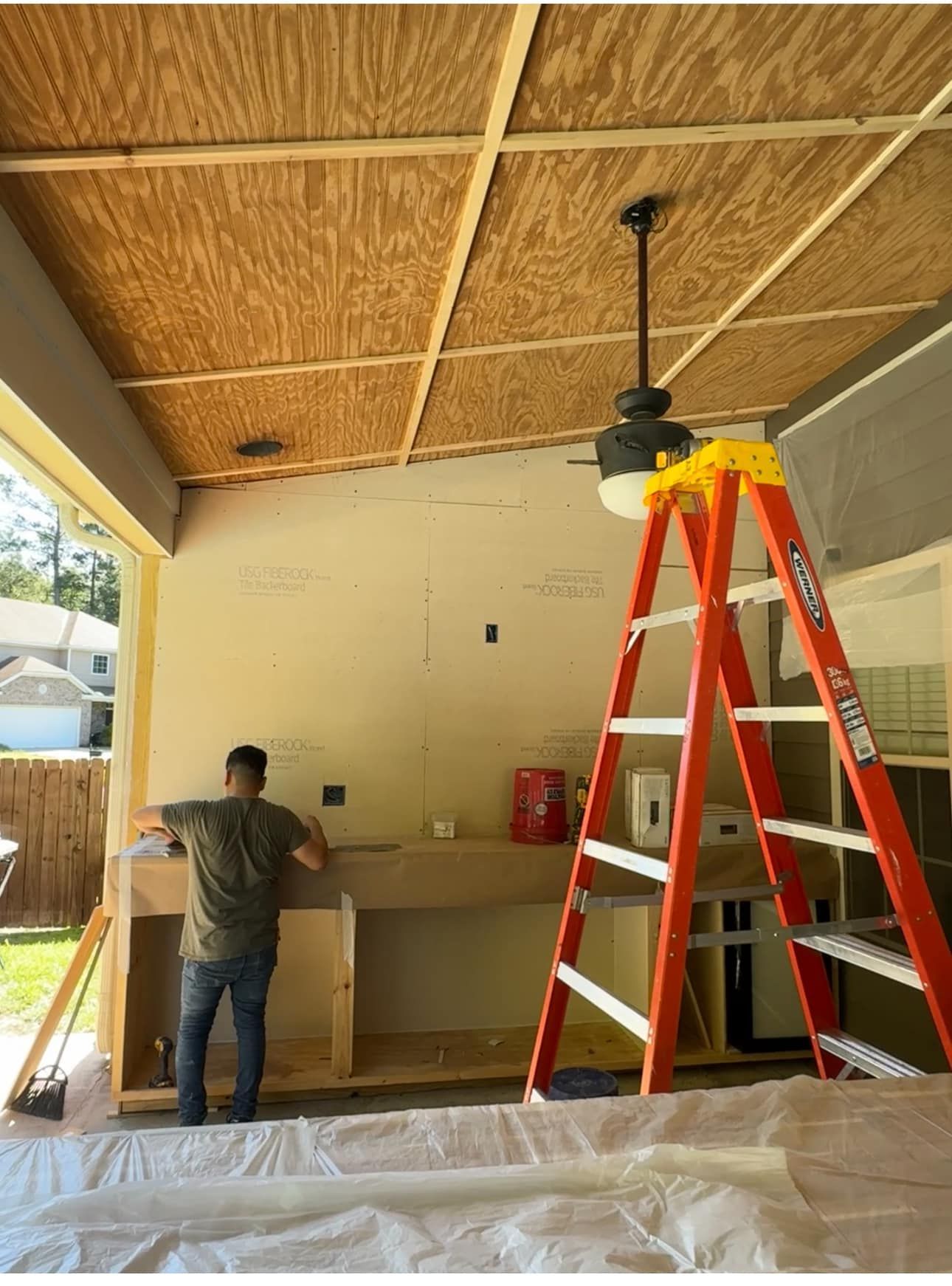 Person working on a covered patio with a red ladder and ceiling fan installation