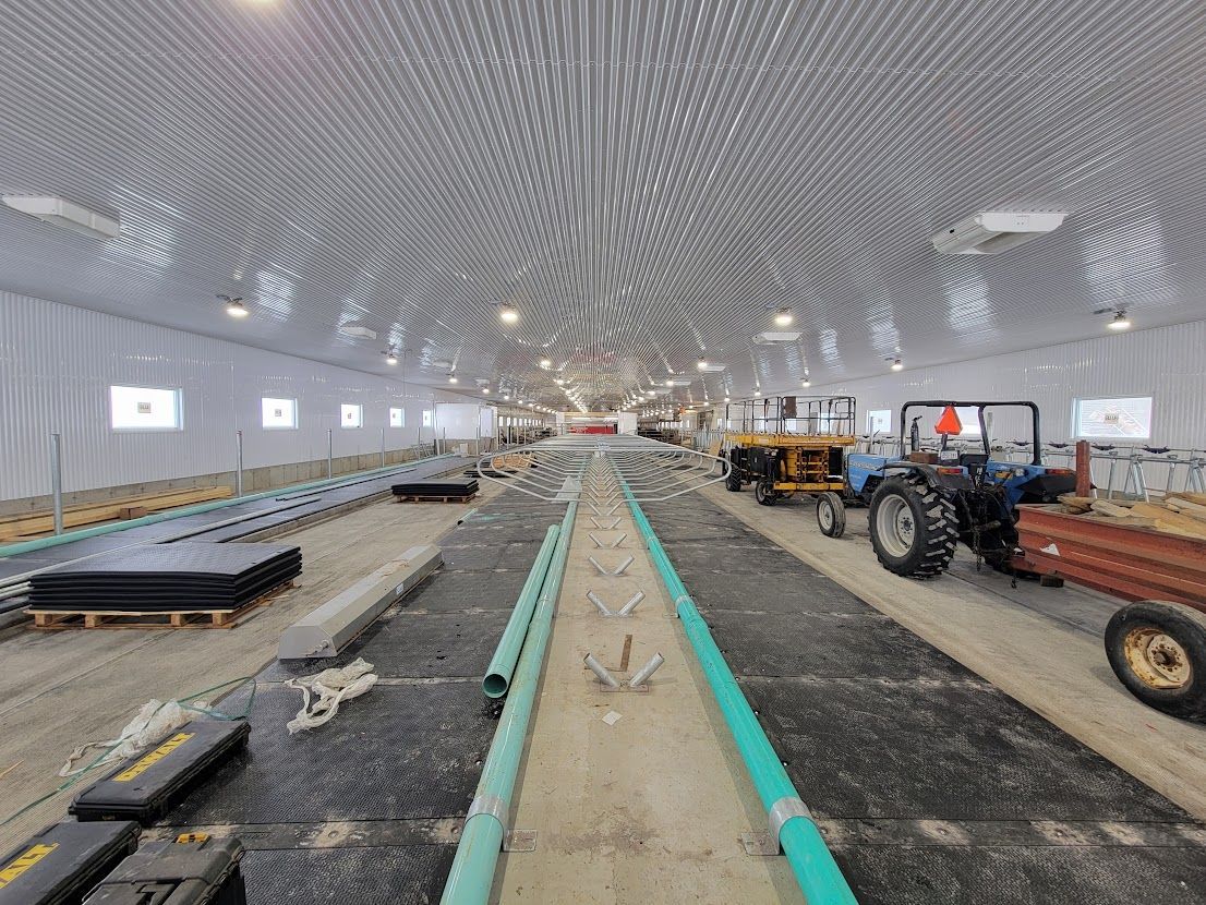 Interior view of a large, bright barn under construction, with tractors and building materials.