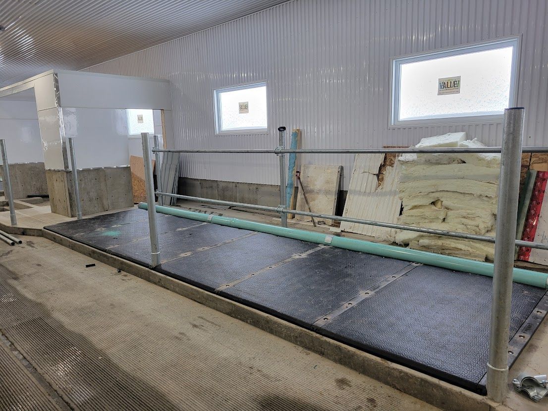 Interior of a livestock barn with a fenced-in area for animals; black mats cover the floor, and the walls are unfinished.