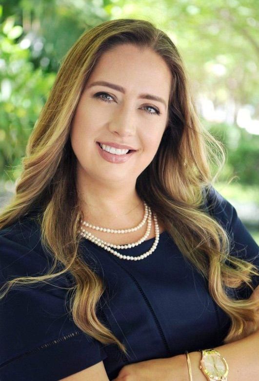 A woman wearing a pearl necklace and a watch is smiling for the camera.