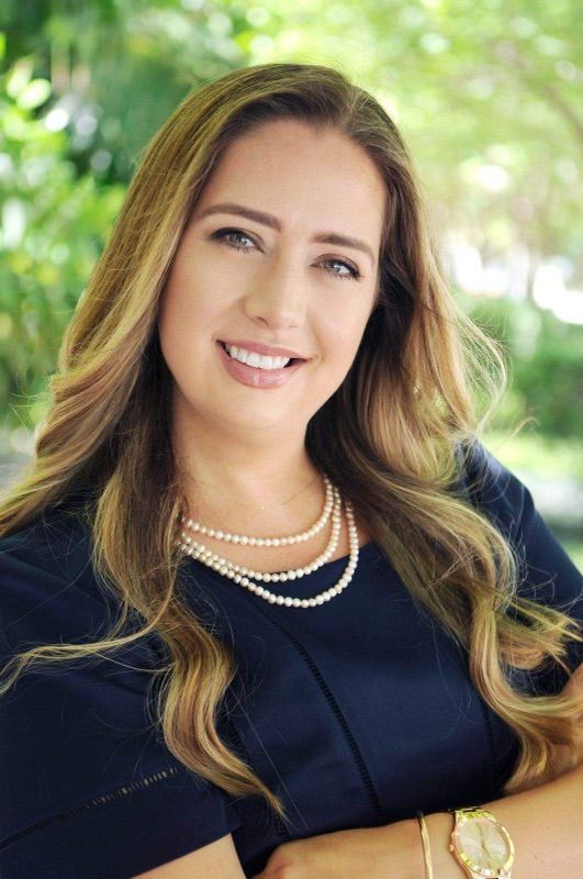 A woman in a blue dress and pearl necklace is smiling for the camera.
