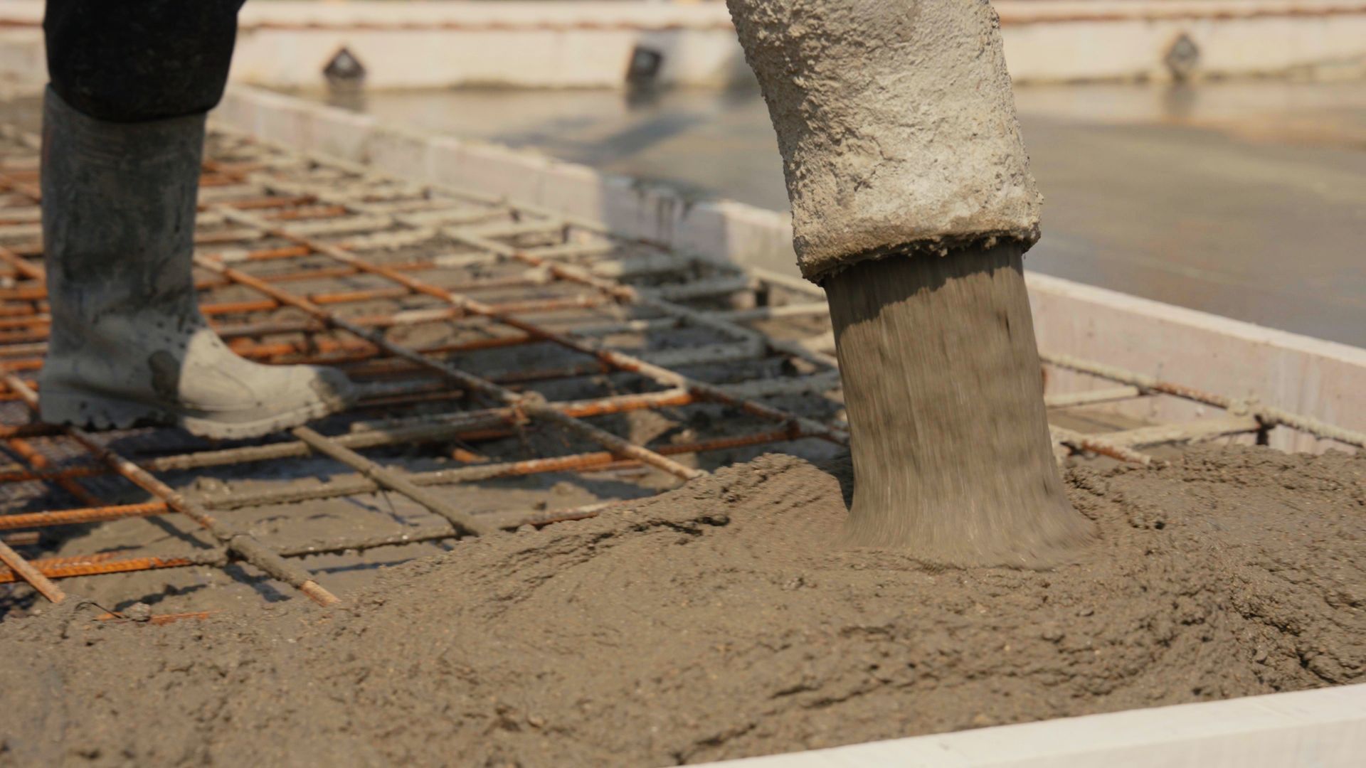 Construction worker pouring wet concrete forming a new slab or foundation on a development site.