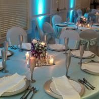 Elegant banquet table with white plates, candles, and teal uplighting in a formal dining room