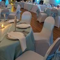 Round banquet tables with white chair covers and teal tablecloths in a decorated event hall.