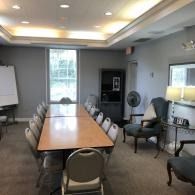 Conference room with long table, chairs, whiteboard, and windowed wall