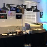 Coffee station with black counter, hanging mugs, and a lit beverage dispenser against a wall of photos