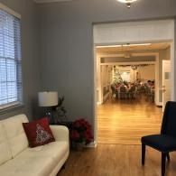 Living room with white sofa, dark chair, lamp, and open doorway to a bright dining room