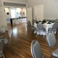 Empty banquet room with round tables, gray chairs, and a white-clothed buffet in the back