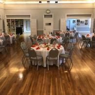 Banquet hall with round, white-clothed tables set for a meal on a polished wooden floor