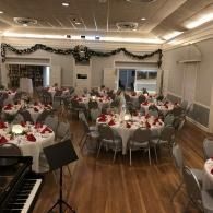Banquet hall with round tables, white chairs, red centerpieces, and a piano in the foreground