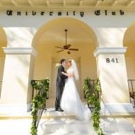 Bride and groom posing on a building entrance with white arches and hanging greenery