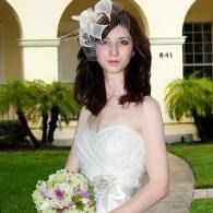 Woman in a white strapless dress holding a bouquet, standing outdoors near an arched building entrance.