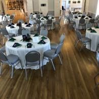 Banquet hall with round tables, white tablecloths, gray chairs, and a polished wood floor