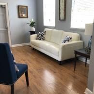 Bright living room with white sofa, blue chair, wood floor, and framed wall art