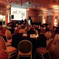 Audience seated in a dim banquet hall watching a presentation on a large screen