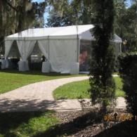 White event tent beside a curved stone path in a grassy, tree-lined outdoor setting