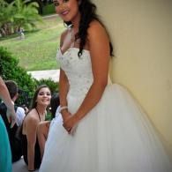 Woman in a white wedding dress smiling, leaning against a column outdoors beside others that are seated