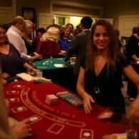 Woman smiling at a casino table with chips, surrounded by other players and green felt tables.