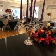 Decorated banquet hall with round tables, black tablecloths, and autumn floral centerpieces