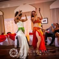 Two dancers in colorful costumes perform with raised arms at an indoor event