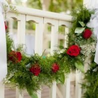Red rose and greenery garland draped across a white gate