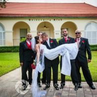 Wedding party posing outdoors with groom holding bride horizontally in front of a building