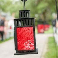 Black hanging lantern with red patterned insert and white hearts, outdoors on a blurred path