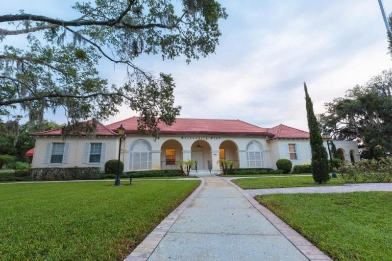 Single-story white house with red roof, arched porch, and a front walkway across a green lawn