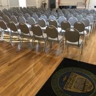Rows of empty metal folding chairs in a hall with a polished wooden floor