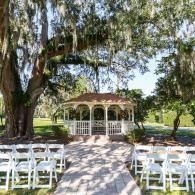 Outdoor wedding gazebo with white chairs and a tree-lined aisle in a sunny garden