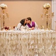 Couple kissing at a decorated wedding table with white flowers and gold accents