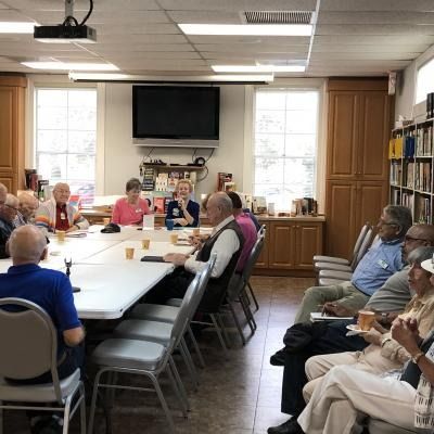 People seated around tables in a bright community room, talking and having a meeting