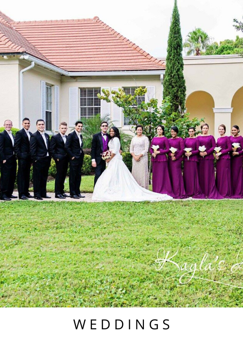 Wedding party posing outdoors in front of a house, with the bride in white and attendants in black and purple.