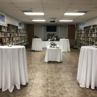 Empty library room with round tables draped in white tablecloths and bookshelves lining the walls