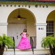 Woman in a bright pink gown standing on the steps of a building with white arches and palm plants