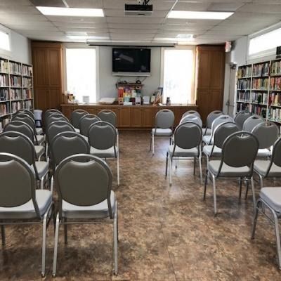Library meeting room with rows of gray chairs facing a front table and wall-mounted TV