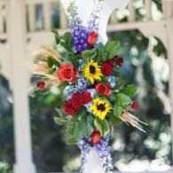 Colorful flower arrangement with sunflowers and red, purple, and blue blooms on a white post outdoors
