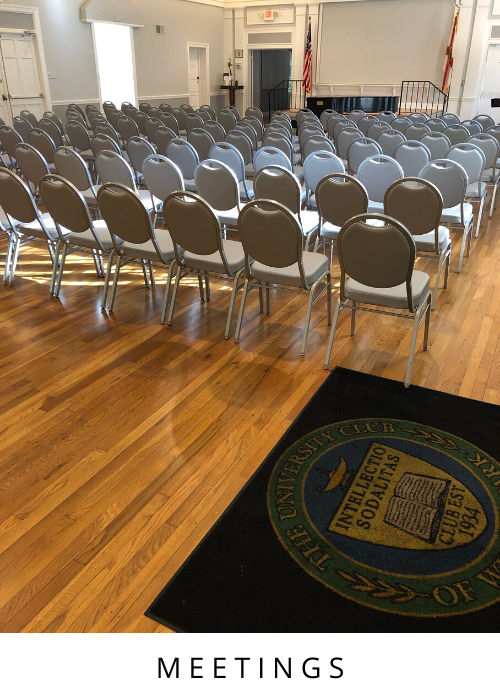 Rows of empty gray chairs in a meeting room with a wooden floor and stage area