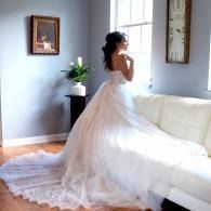 Bride in a white gown standing by a white sofa in a bright living room