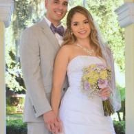 Wedding couple posing outdoors, bride in white dress holding bouquet, groom in light gray suit.